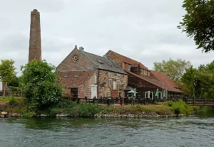 Mill converted to pub with large chimney to the left and across a body of water