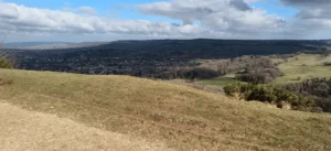View from top of hill over to a wooded hill on the other side of the valley and fields below