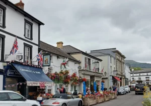 A high street with a pub with lots of flowers and people sitting outside