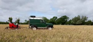 Landrover pulling a brush harvester in a meadow