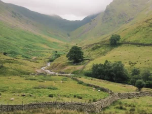 A green valley with steep sides, a river in the middle and a clouded mountain top on the left