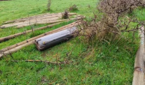 Fence posts laying flat on a field next to a post rammer