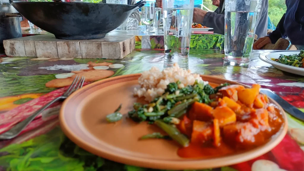 Curry, rice and greens on a plate with a glass of water in the background