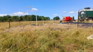 A tarpaulin with seed on in a field and a landrover driving past pulling a seed harvester