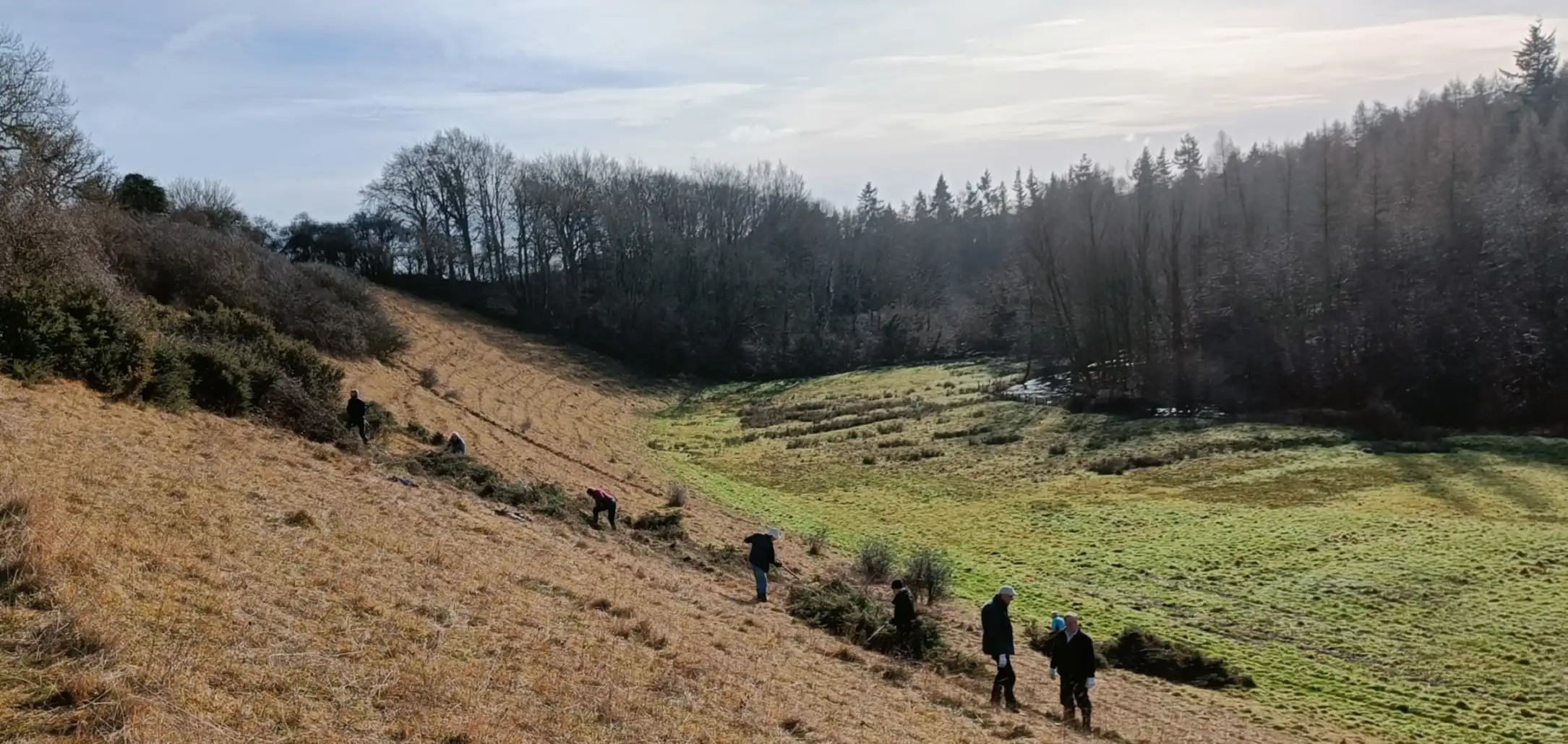 A steep bank down to a valley floor with river in the background. People working on the slope.