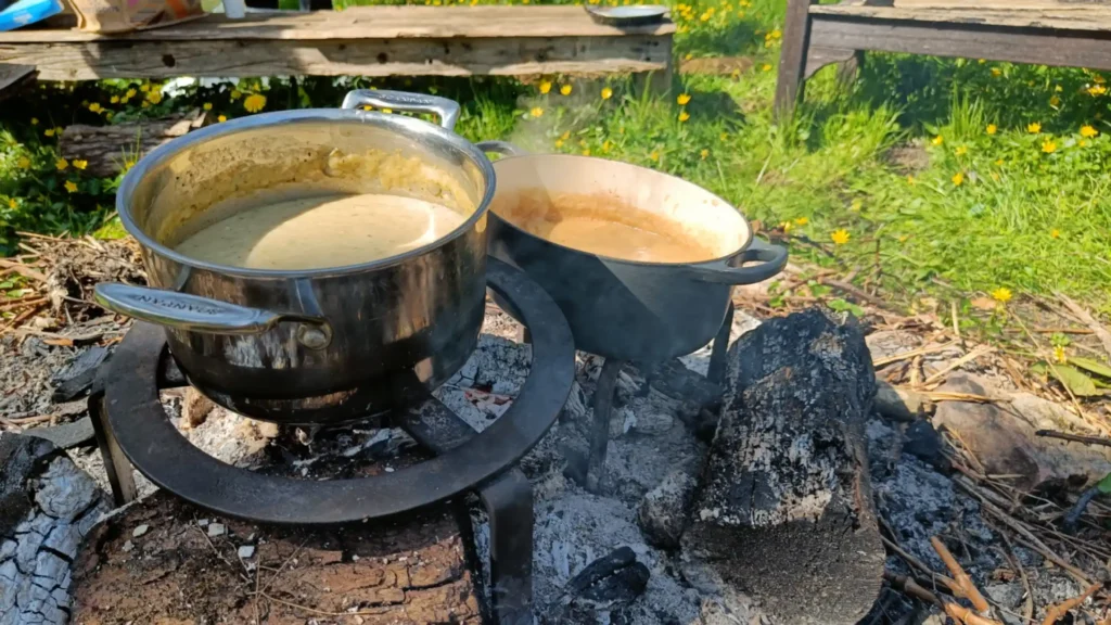 Two pots of soup cooking on an open fire in a meadow