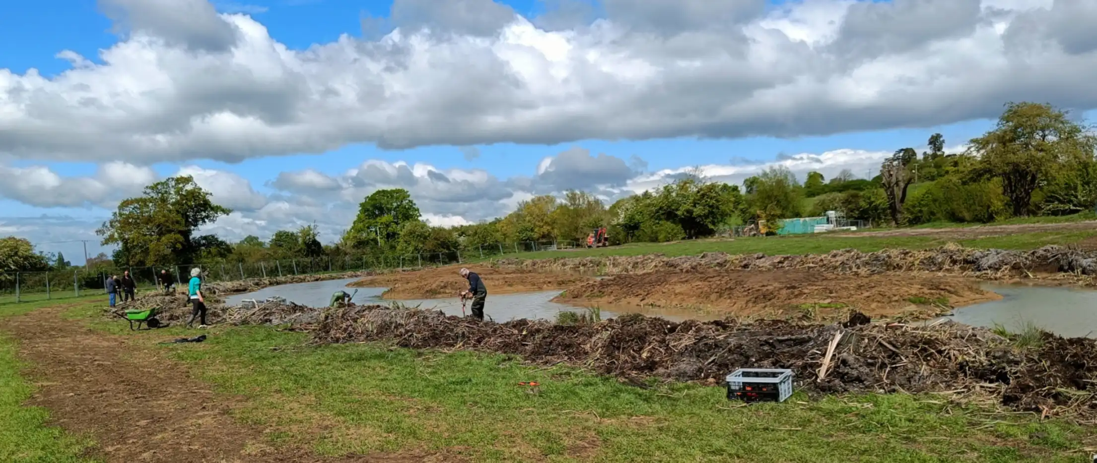 A large pond with people standing on the bank planting