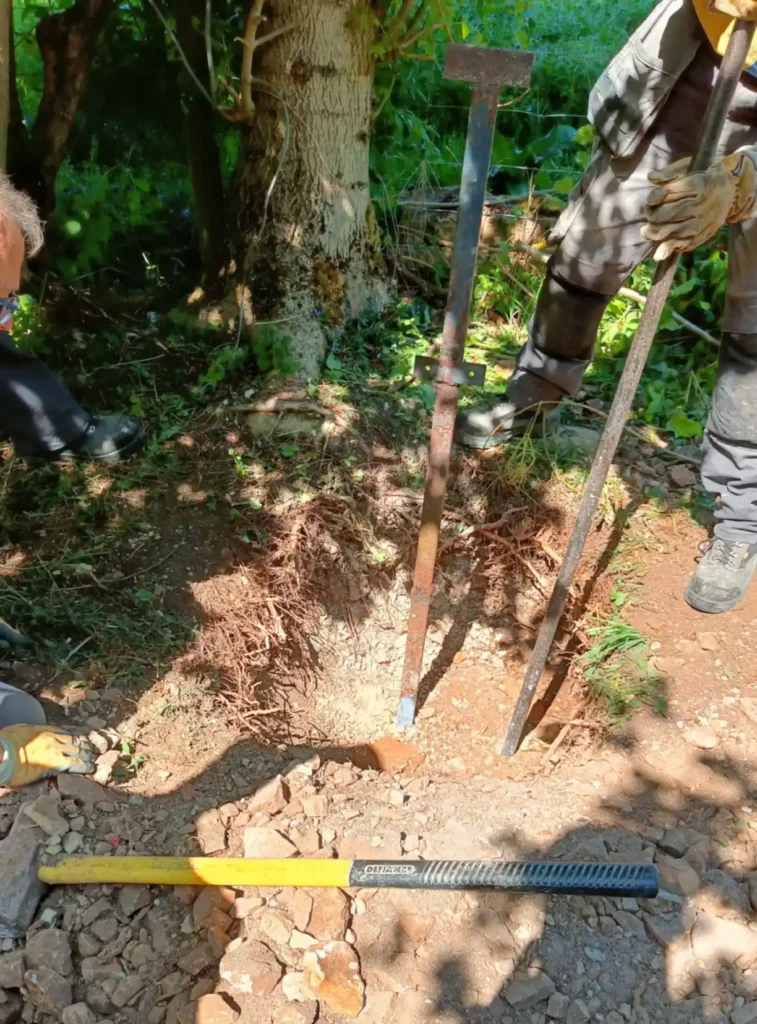 A pole stuck in the ground with a large hole dug around it. Man breaking stones with a wrecking bar