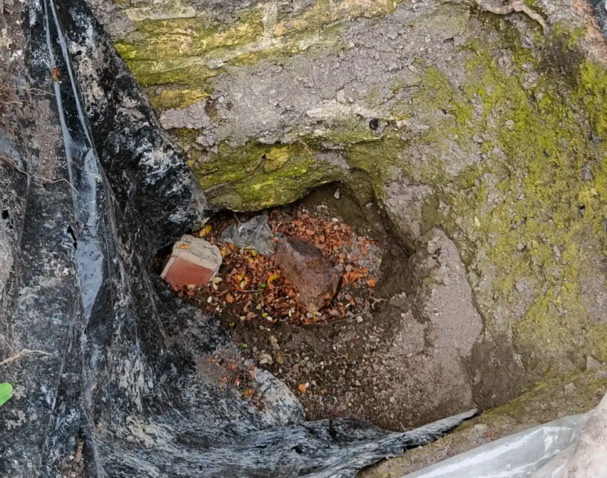A deep trial pit next to a stone wall
