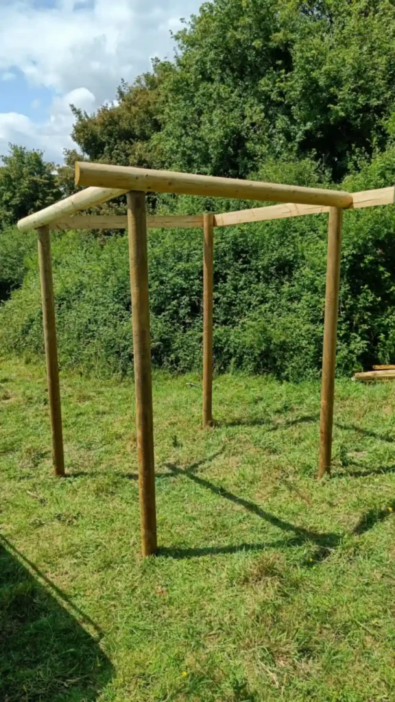 Four upright posts in the ground in a field. They are in a small square and the tops of the posts have a rail around