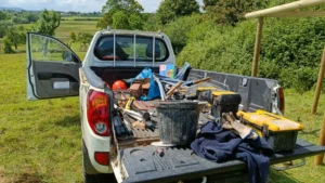 A white truck in an orchard with the tailgate down and lots of equipment on it.