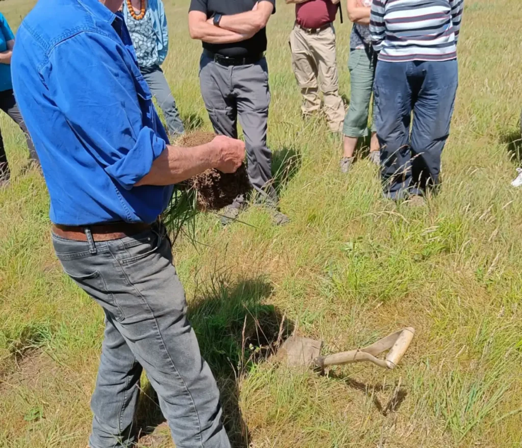 I man showing a group of people a wedge of soil he's just dug up