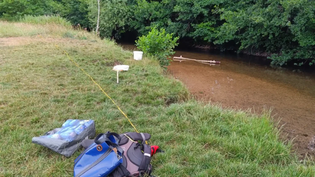 a rope on the ground about a meter back from a riverbank and bags, net and bucket next to it