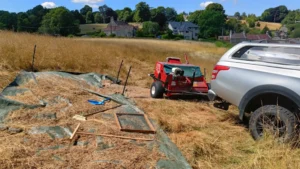 A truck pulling a seed harvester next to a tarpaulin with seeds drying
