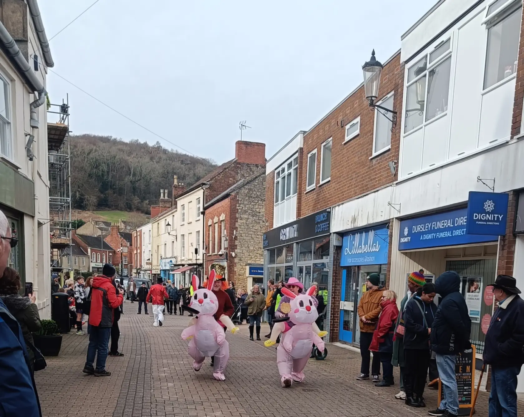 A high street with hill in the background and a pancake race down the street with two people in fancy dress as ponies
