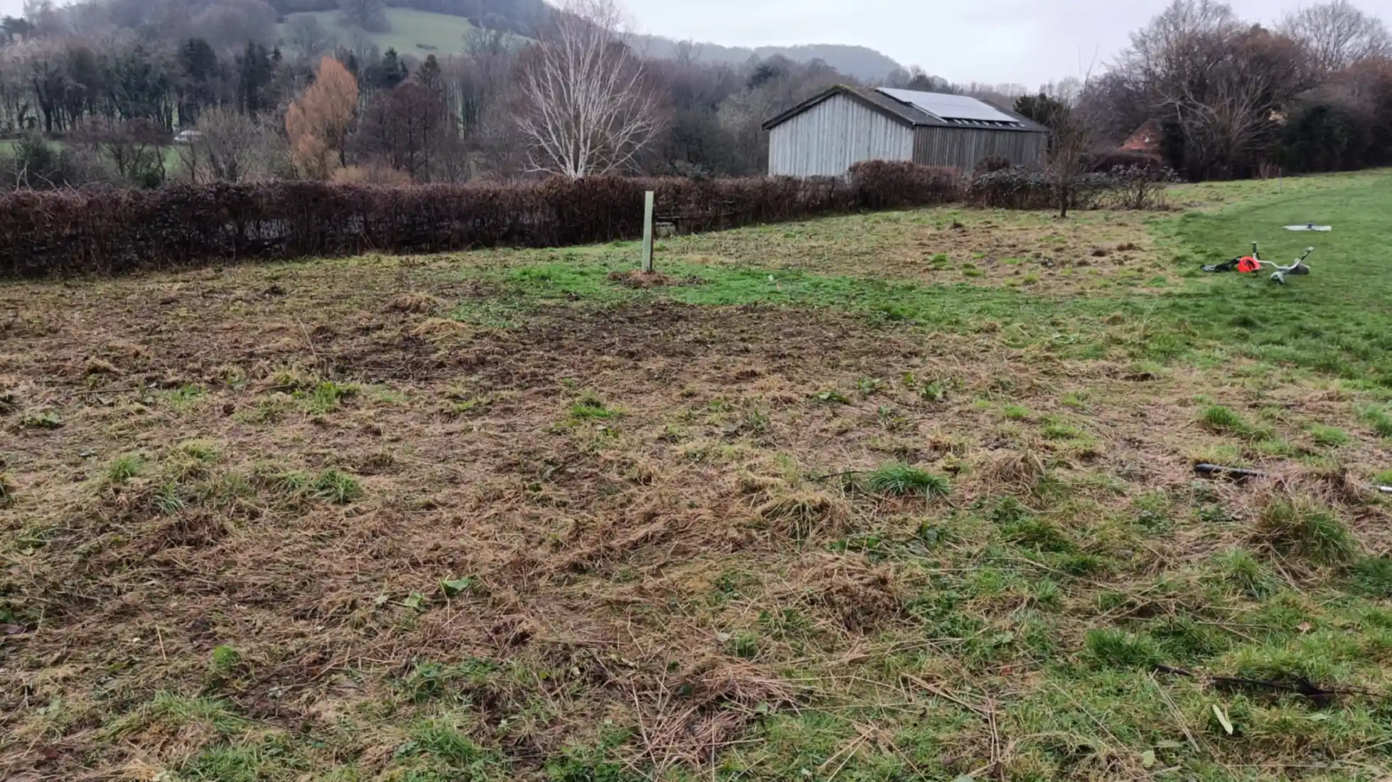 The corner margin of a sports field, cut and raked. Brushcutter lying to the side/